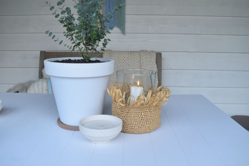 windlichthoes van raffia op tafel naast plantenpot