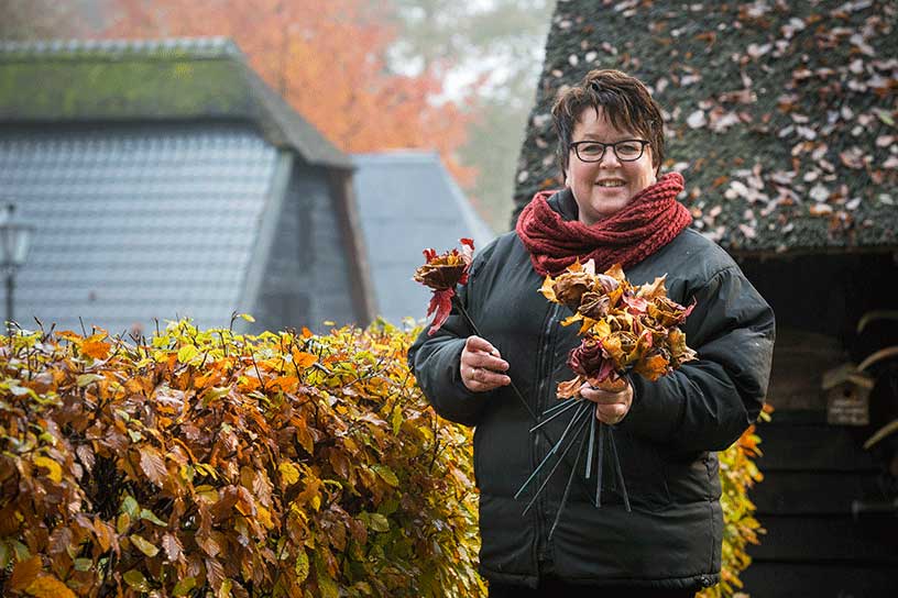 vrouw bij heg met rozen van herfstblad in handen